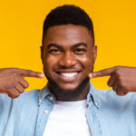 man in a denim jacket pointing at his smile