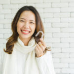 Brunette woman in a sweater smiles while holding her Invisalign aligners in Jefferson City, MO