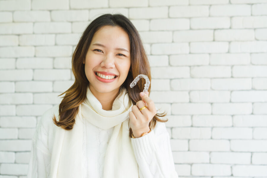 Brunette woman in a sweater smiles while holding her Invisalign aligners in Jefferson City, MO