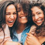 three young women hug and smile showing off their white, straight teeth