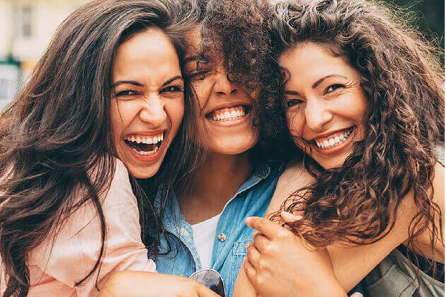 three young women hug and smile showing off their white, straight teeth