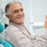 senior man gives a thumbs up in the dentist chair after a good checkup
