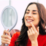 woman wearing a red sweater holds a mirror up to inspect her gums