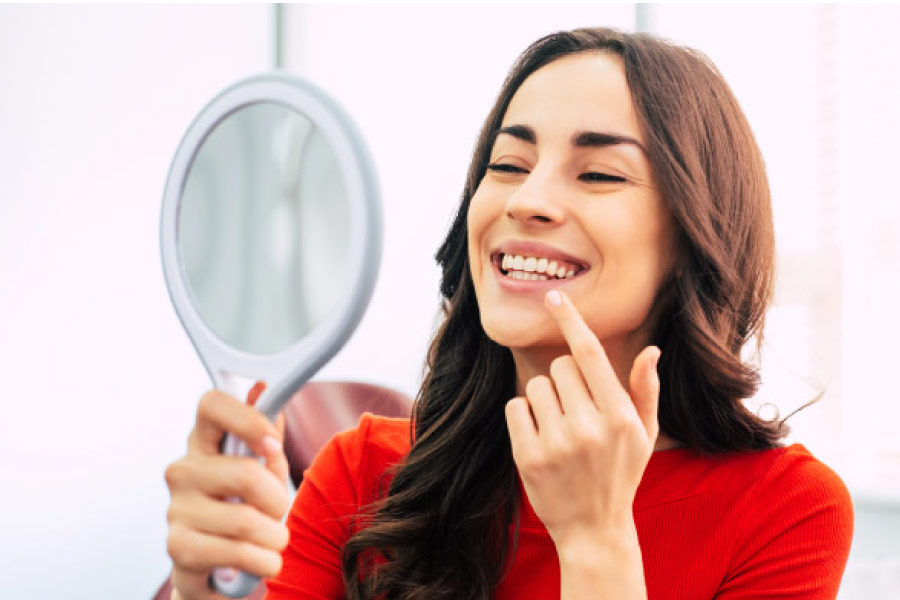woman wearing a red sweater holds a mirror up to inspect her gums