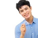 young man smile and holds up his clear aligner to straighten his teeth