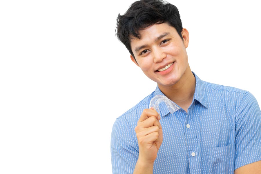 young man smile and holds up his clear aligner to straighten his teeth