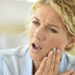 blond woman holds her jaw with tooth sensitivity
