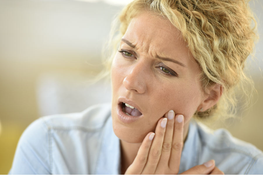 blond woman holds her jaw with tooth sensitivity